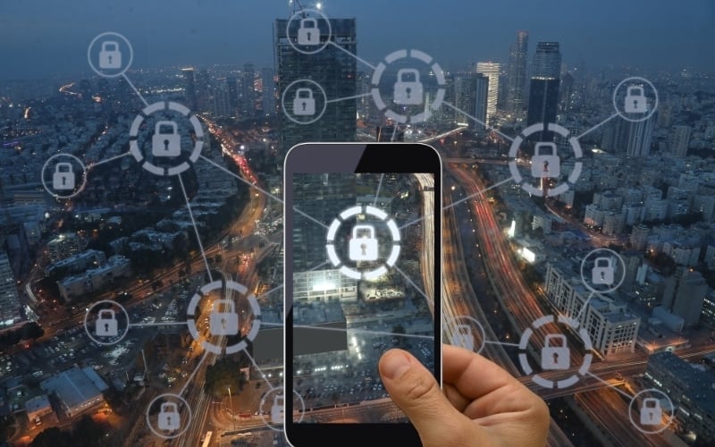 Hand holding smartphone displaying digital security icons over a cityscape, symbolizing cybersecurity and digital safety in Brisbane, Ipswich, and Logan.